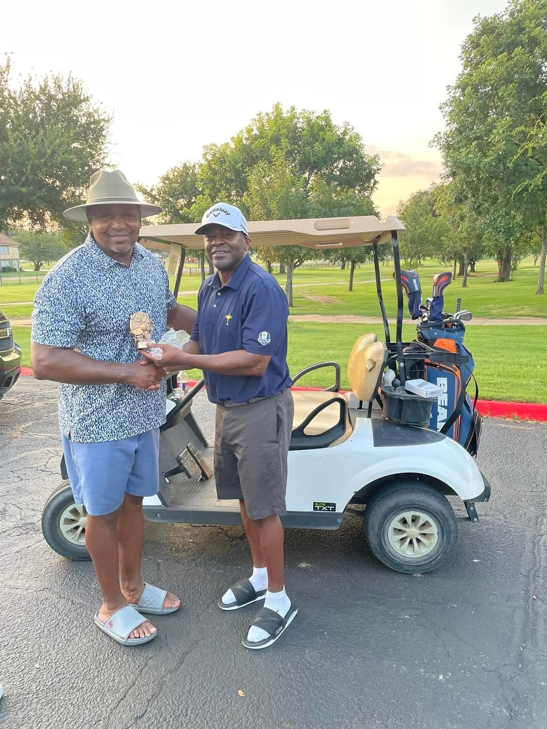 Two friends shaking hands as one receives the Longest Drive trophy by a golf cart