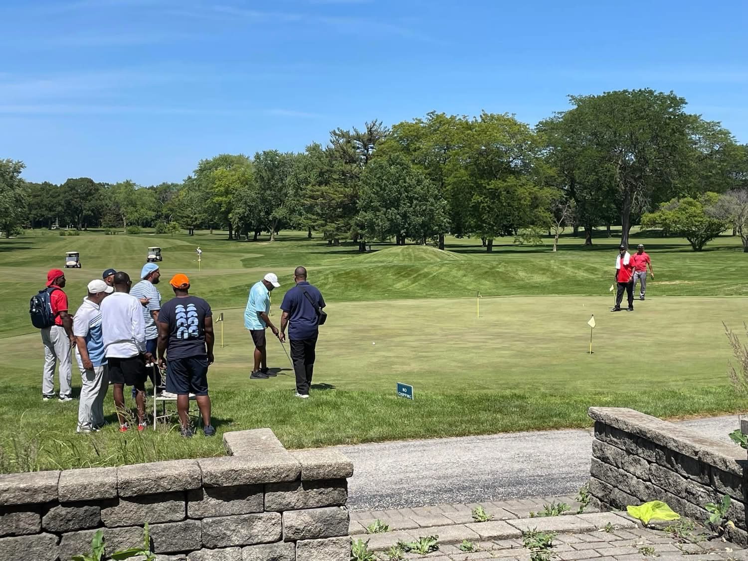 A group of friends gathered on the practice putting green on a sunny morning