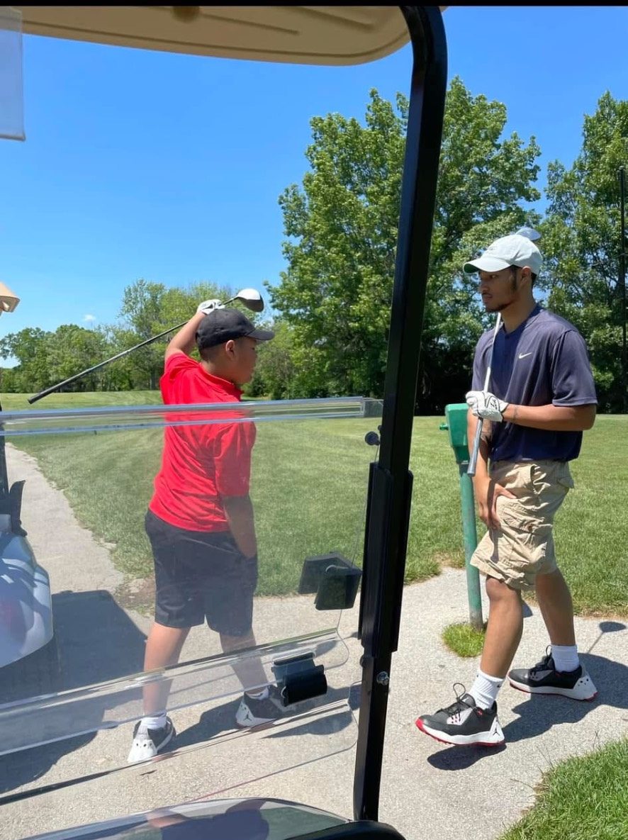 A father and son taking practice swings together at a tee box