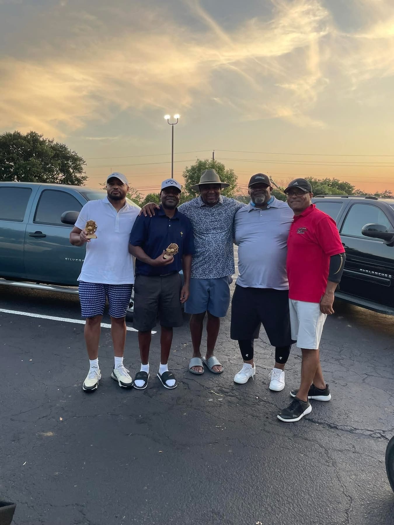 Five friends arm-in-arm in the parking lot at sunset after a round