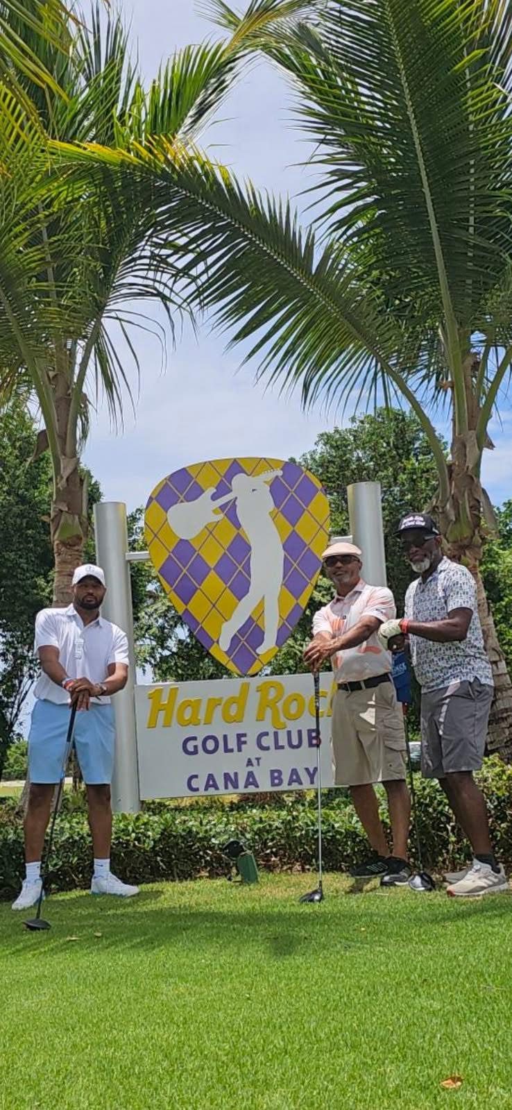 Three golfers posing under palm trees by the Hard Rock Golf Club sign in Punta Cana