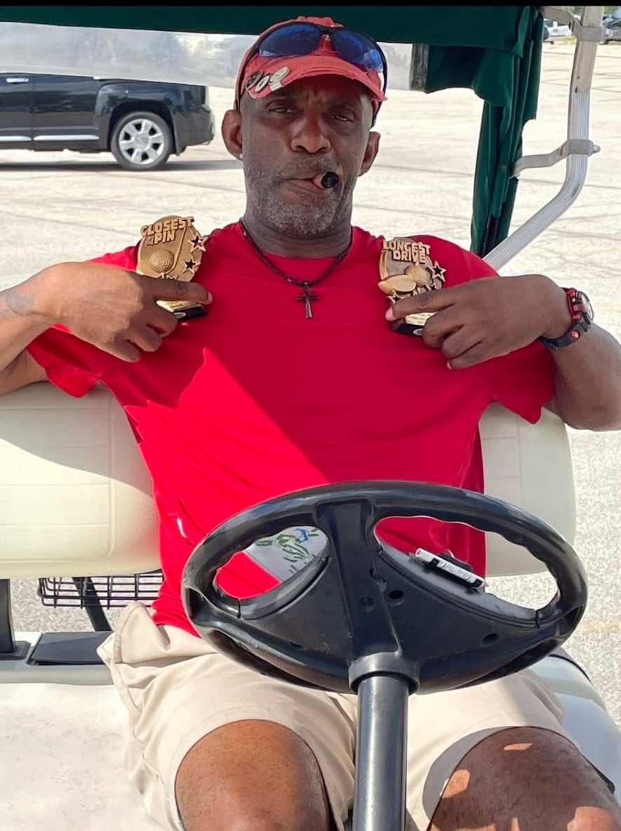 A golfer in a red shirt holding the Closest to the Pin and Longest Drive trophies