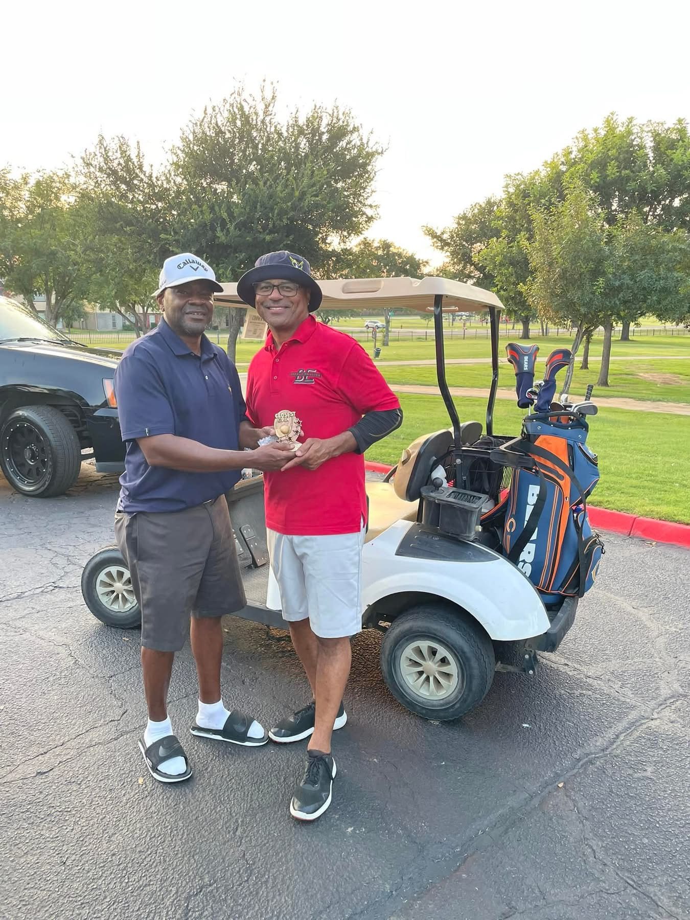 Two friends celebrating with the Closest to the Pin trophy beside a golf cart