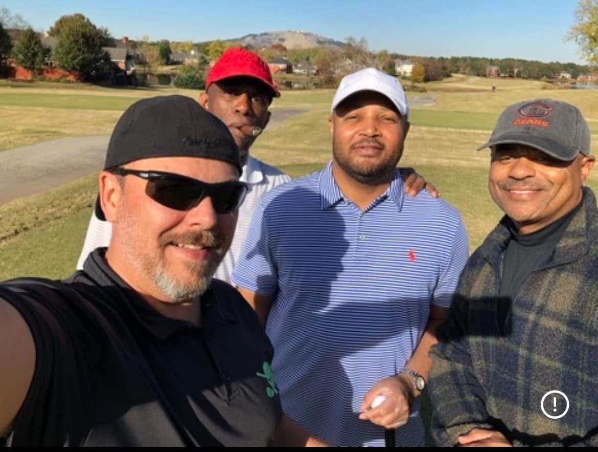 Four friends posing for a selfie on a fall fairway with mountains in the distance